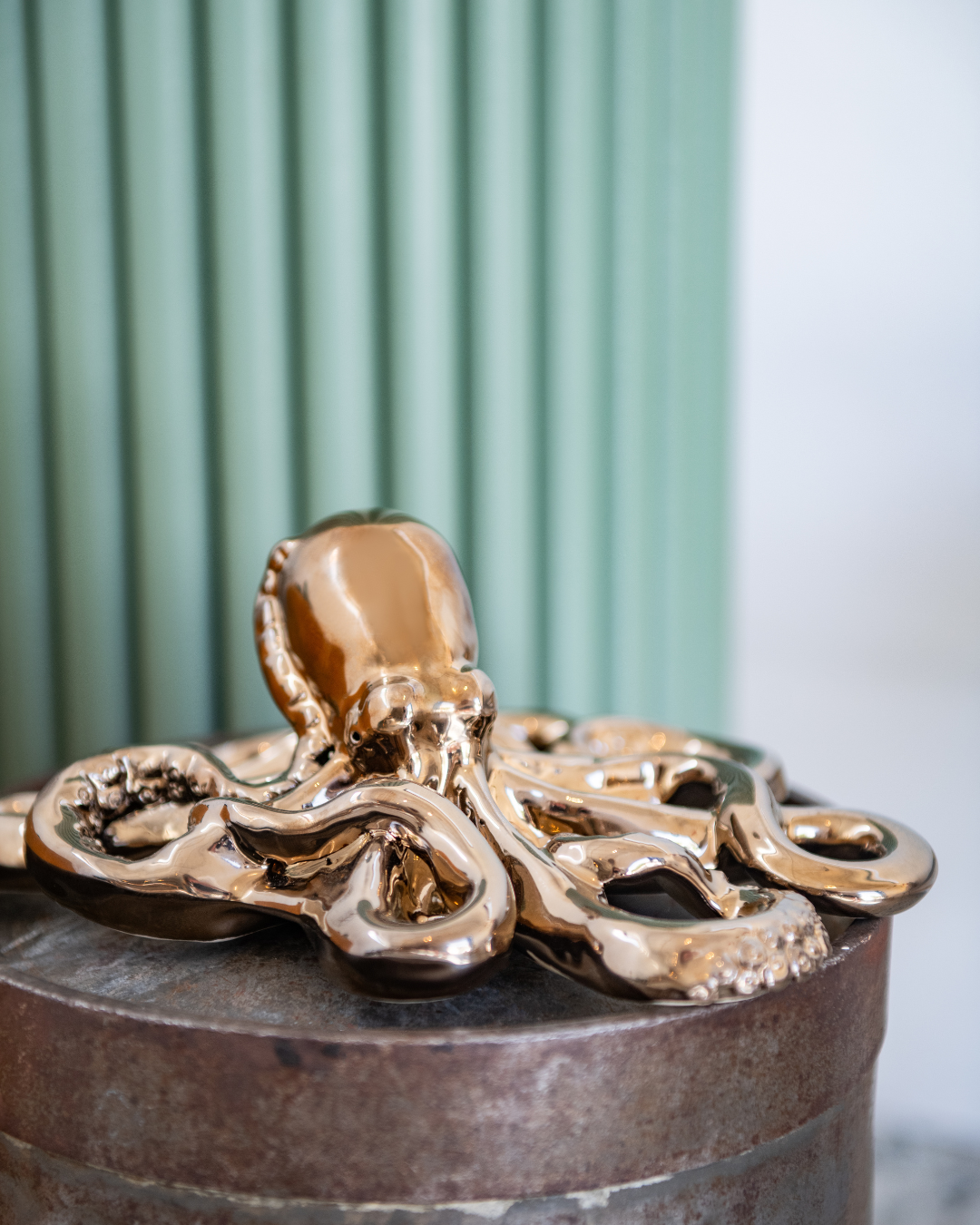 Bronze octopus sculpture on a cylindrical metal base with a green and white background