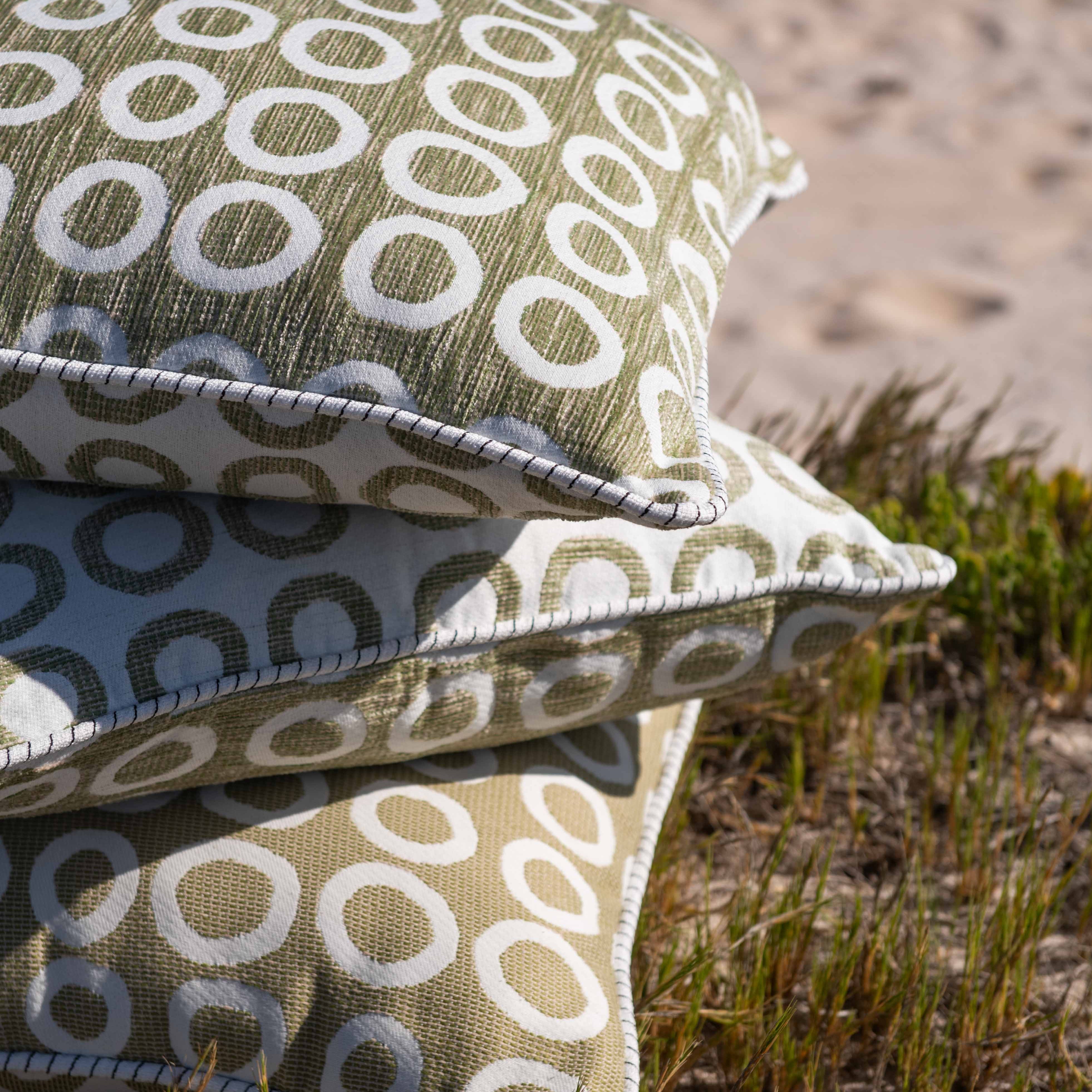 Stack of patterned pillows on a sandy surface with grass