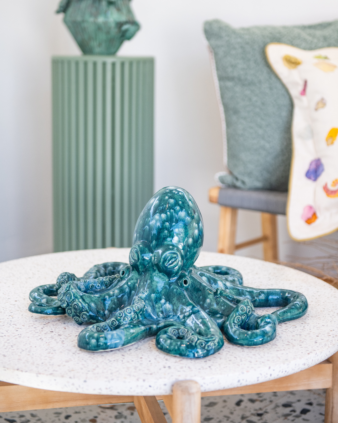 Blue octopus sculpture on a white table with a colorful pillow and green vase in the background