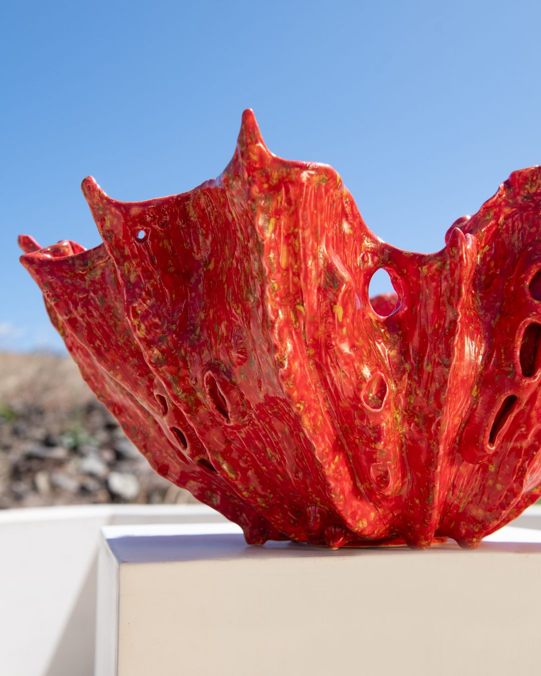 Red ceramic sculpture on a white pedestal with a blue sky background
