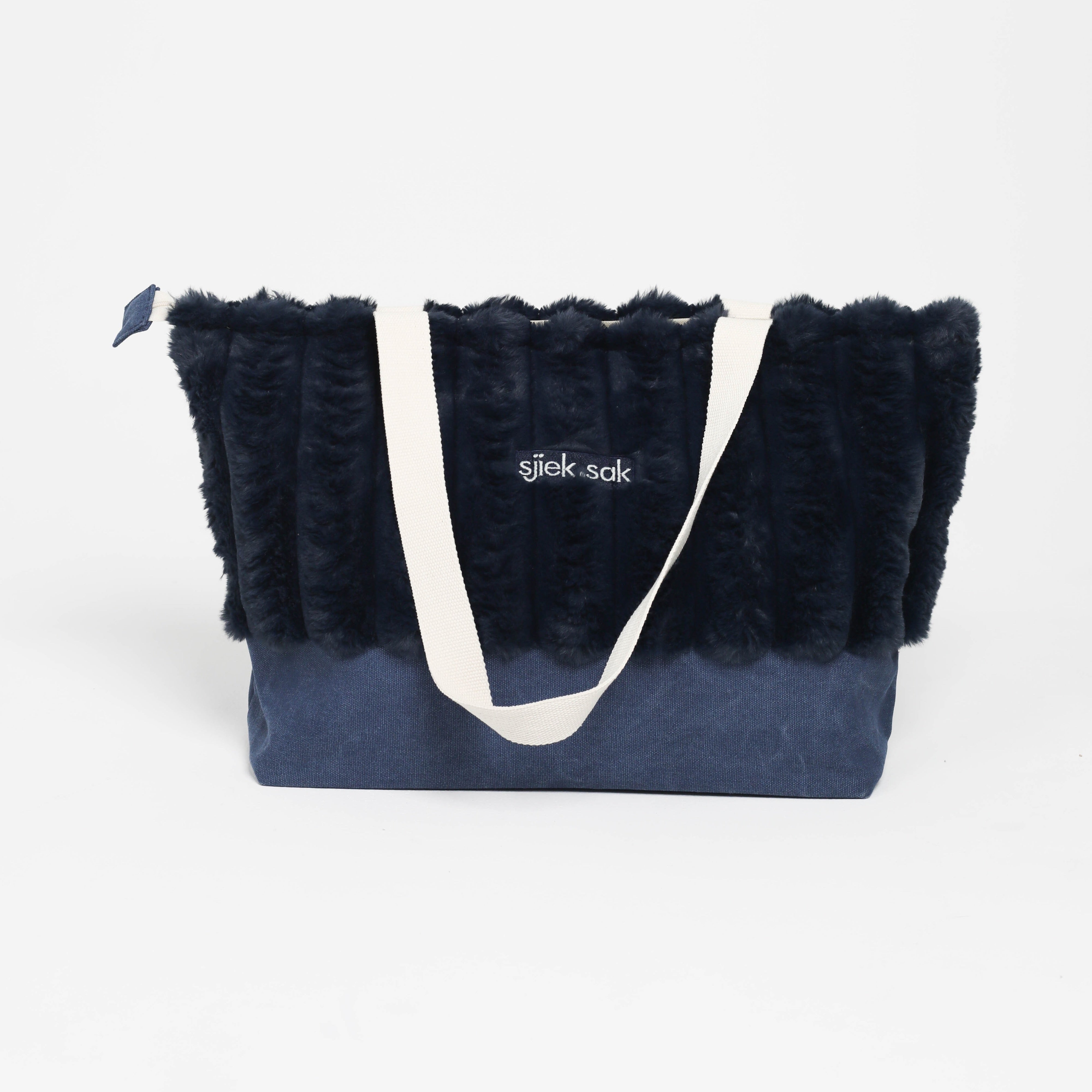 Navy tote bag with black fur trim and white handle on a light gray background